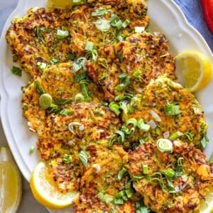 Healthy zucchini patties made with feta, fresh herbs, and grated vegetables, served on a rustic plate with yogurt sauce.