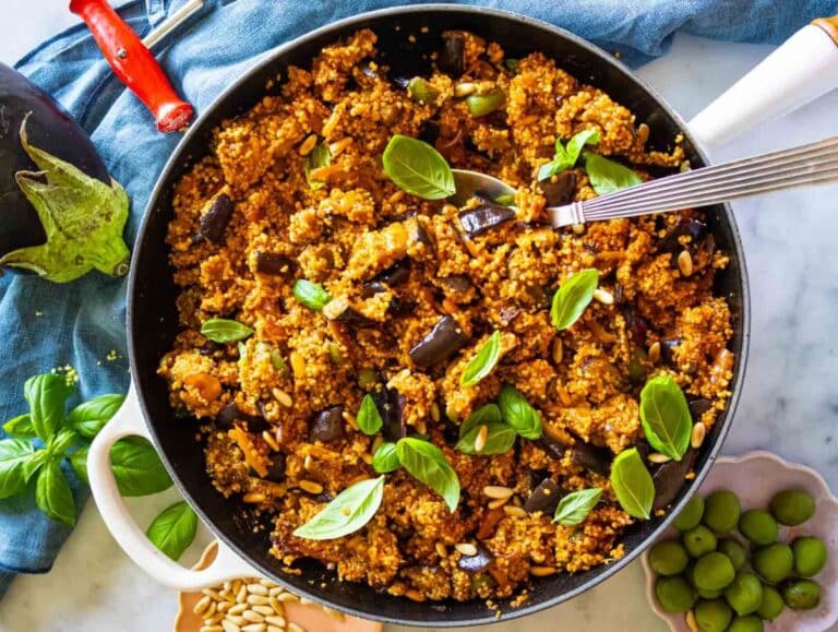 Mediterranean couscous salad served in a skillet, garnished with fresh basil and ready to eat.