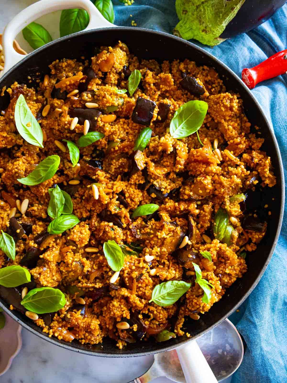 Overhead view of Mediterranean couscous salad served in the skillet with fresh basil and pine nuts.