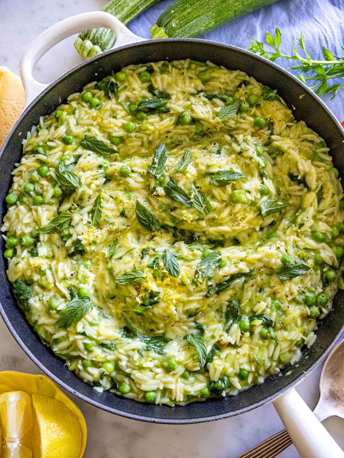 Overhead view of lemon orzo with zucchini, peas, and spinach in a white serving bowl.