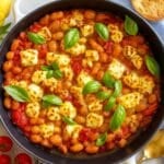 Saucy butter beans in a skillet with cherry tomatoes, and feta, topped with basil.