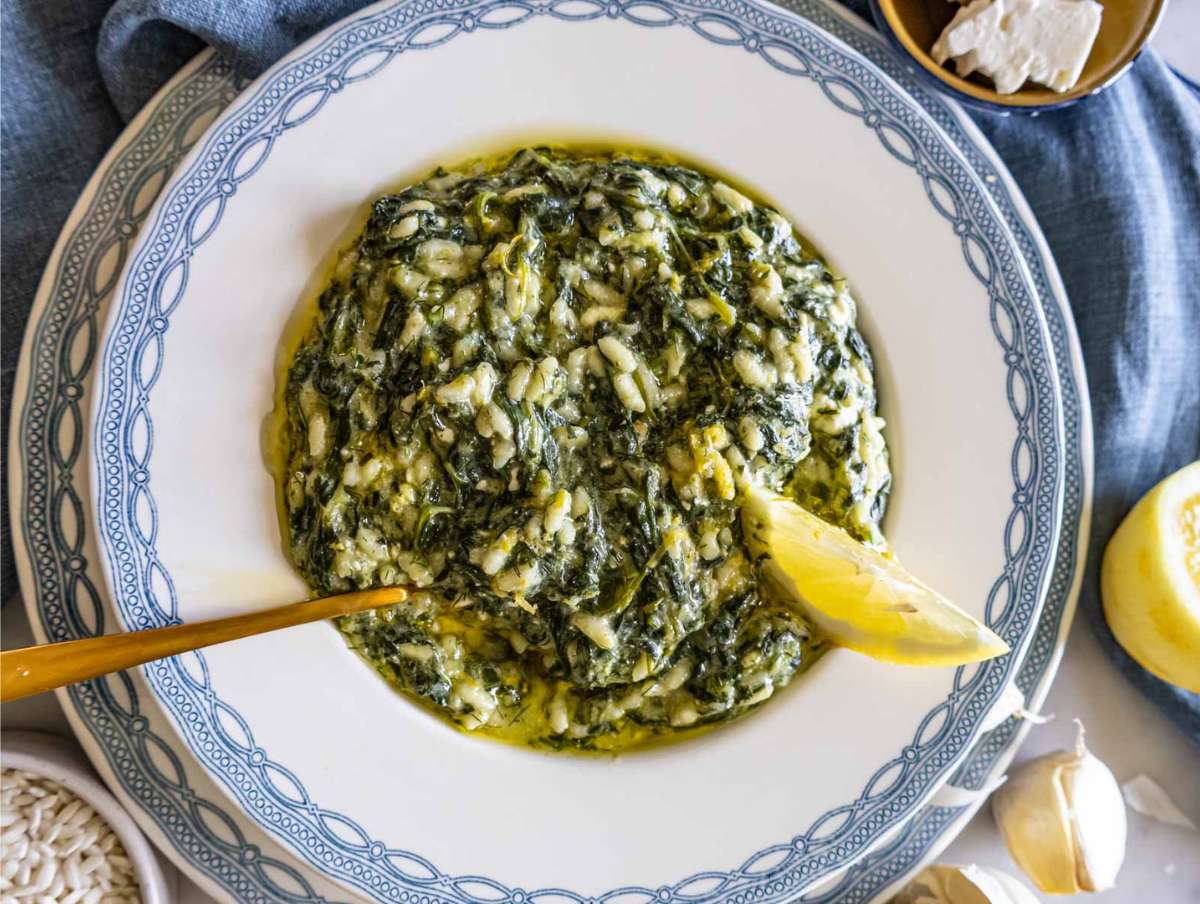 Spanakorizo served on a white and blue plate with lemon and olive oil.