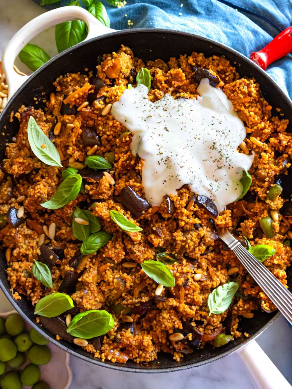 Top down of Mediterranean couscous salad with yogurt, roasted eggplant, olives, and capers in a cast iron skillet.