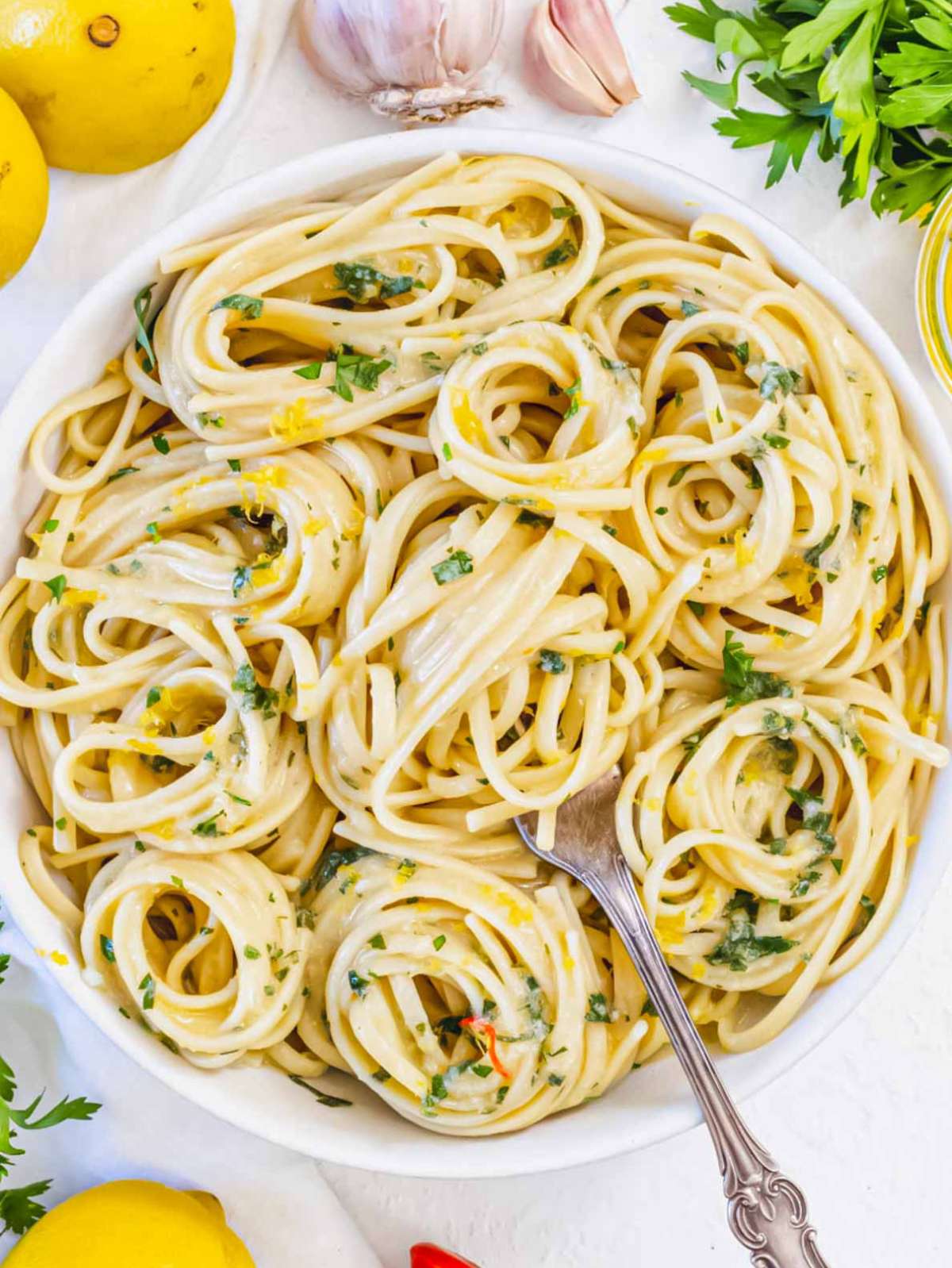 Top-down view of a bowl of lemon pasta without cream, with visible parsley, olive oil, and grated lemon zest top.