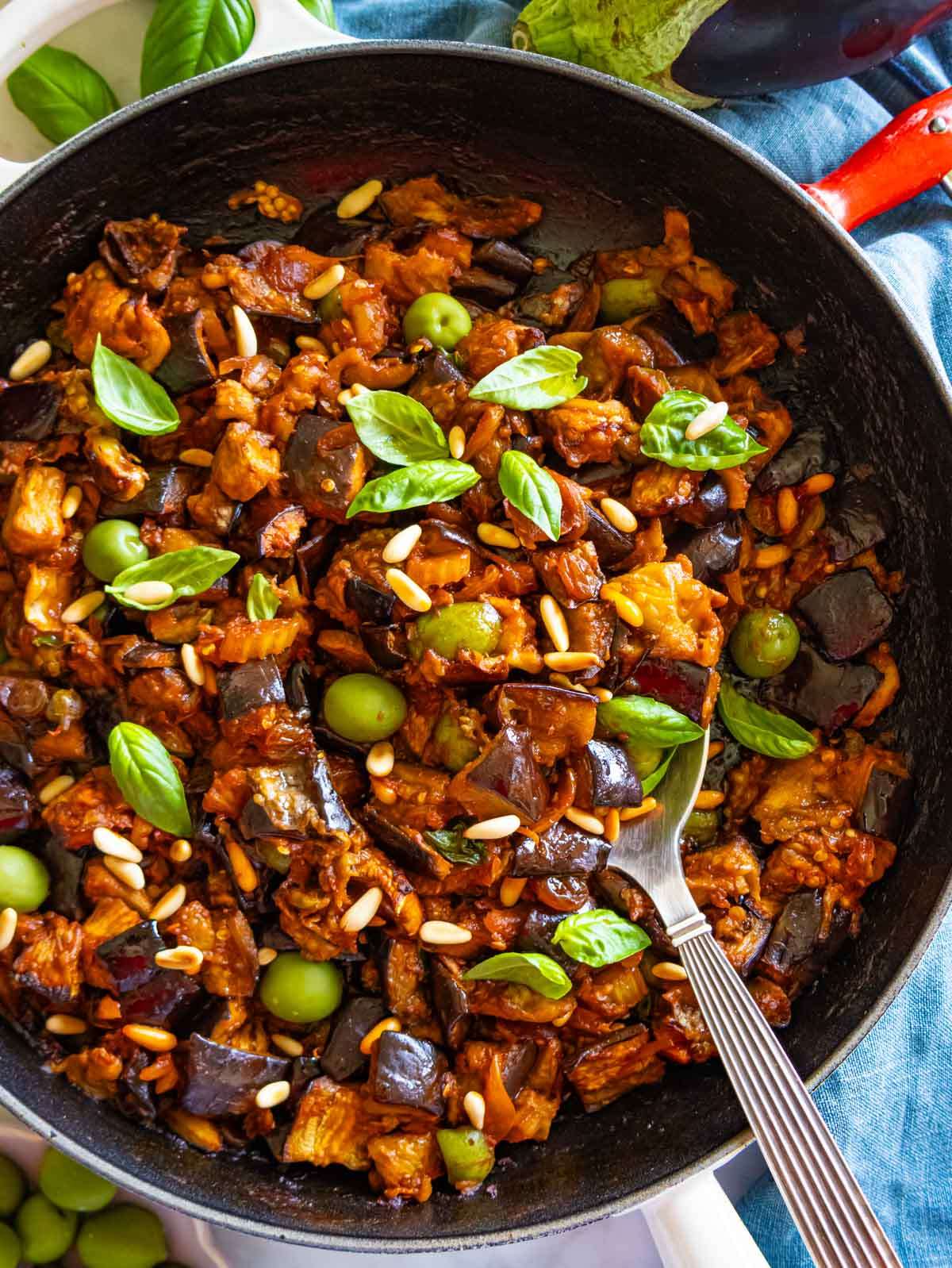 Top-down view of authentic Sicilian caponata served in cast iron skillet with basil.