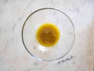 Whisking olive oil, vinegar, lemon juice, and dried oregano in a bowl to create a light vinaigrette.