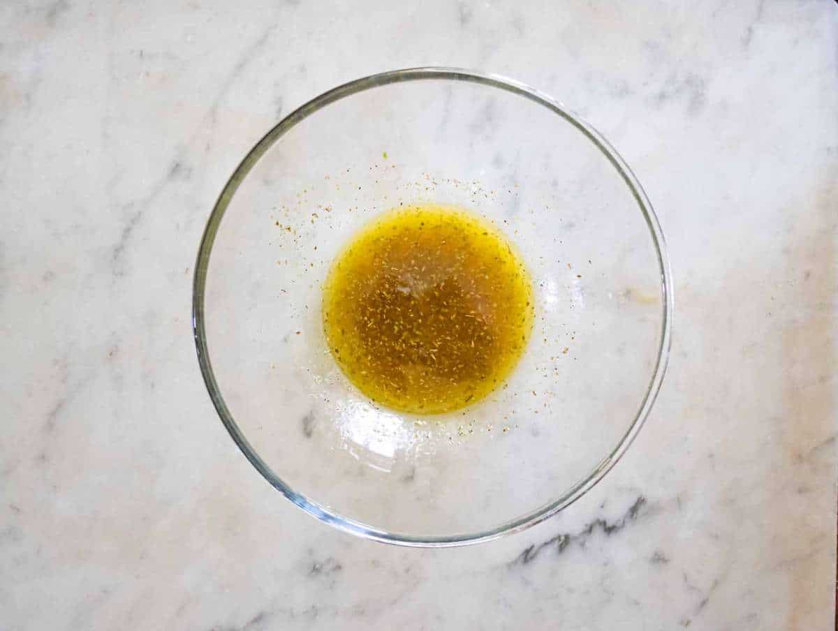 Whisking olive oil, vinegar, lemon juice, and dried oregano in a bowl to create a light vinaigrette.
