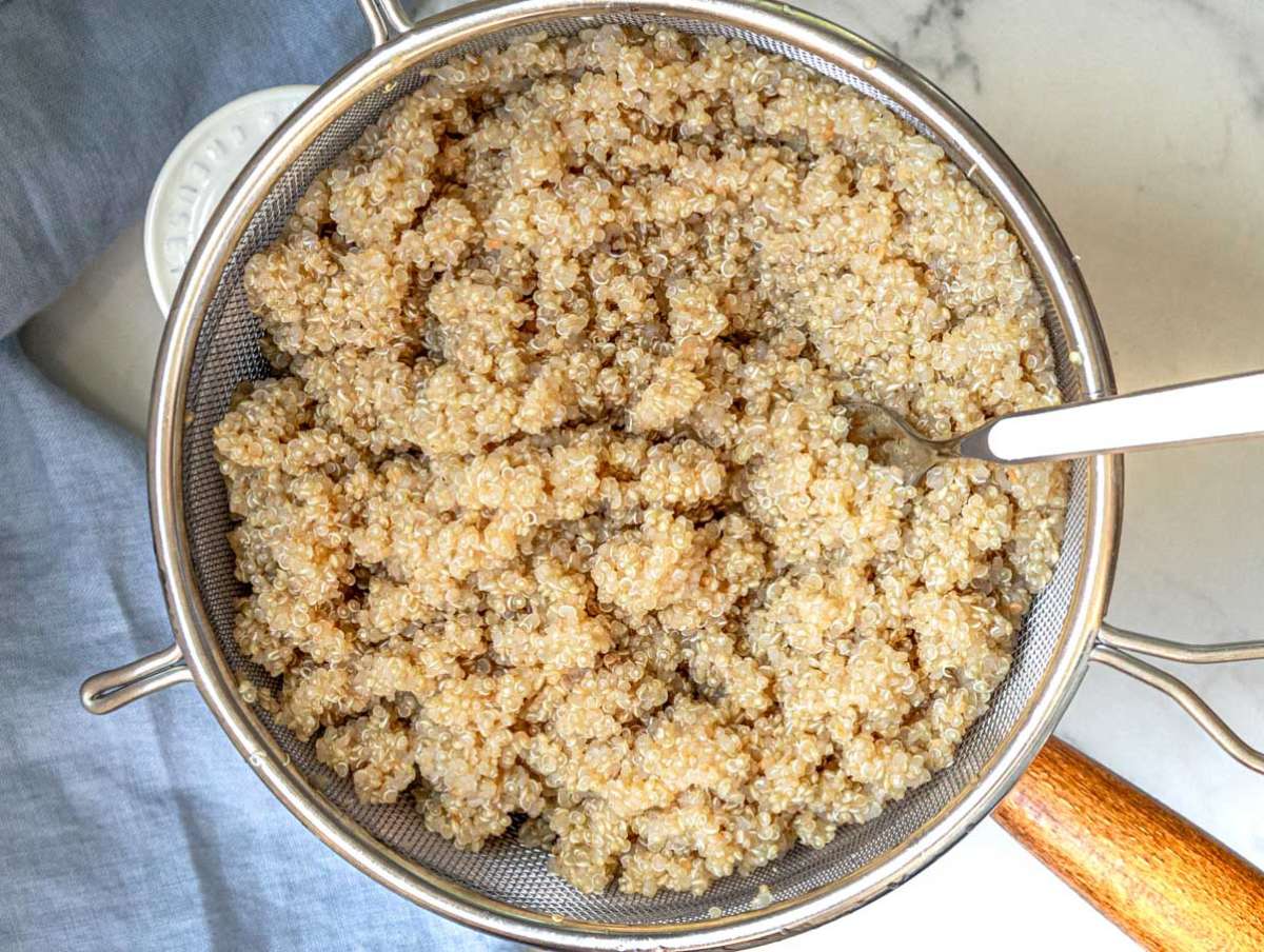 White quinoa cooking in a pot and cooling in a fine mesh strainer, step one for making a heart-healthy kale quinoa salad