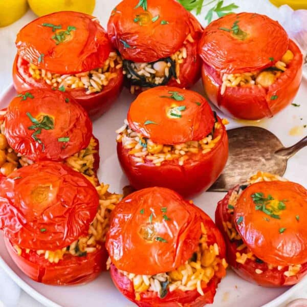 baked stuffed tomatoes arranged on a white platter for a healthy and plant-based Mediterranean recipe.