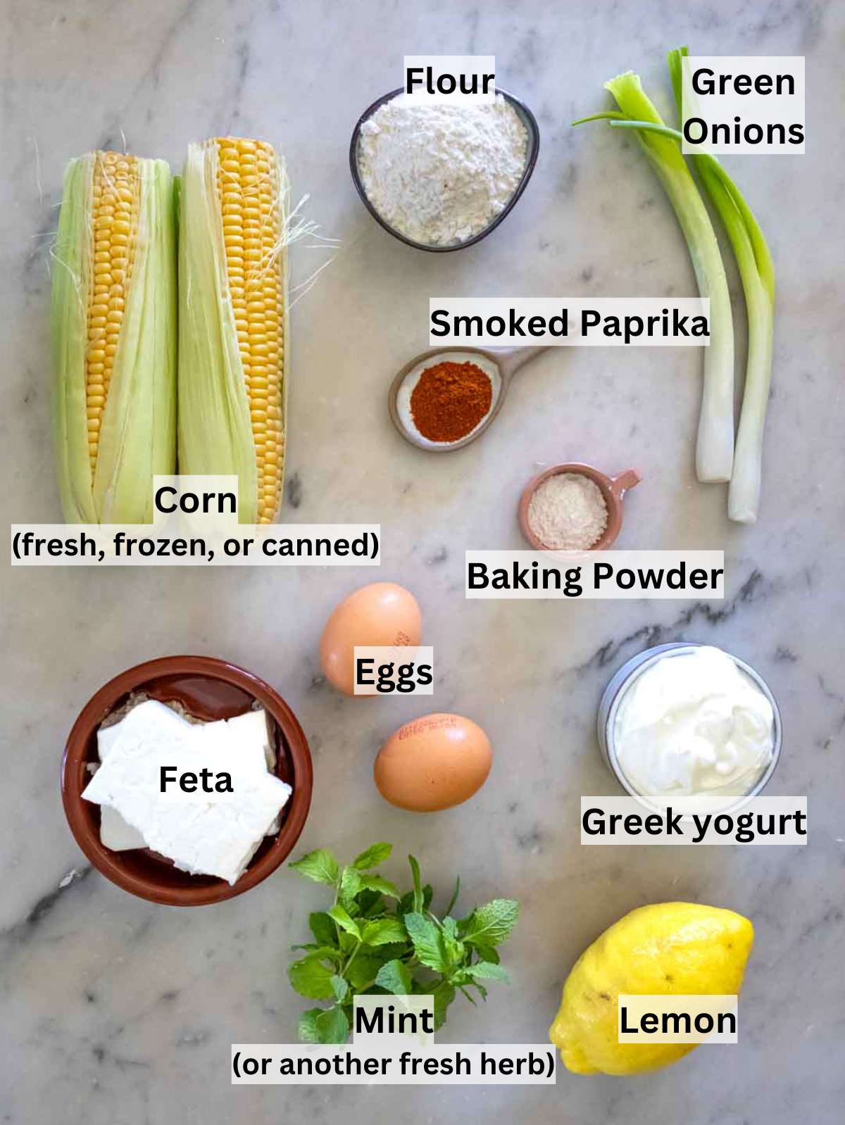 All ingredients for corn fritters laid out on a wooden board with bowls and measuring cups.