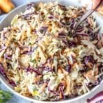 Bowl of healthy coleslaw with Greek yogurt surrounded by ingredients on a wooden table.