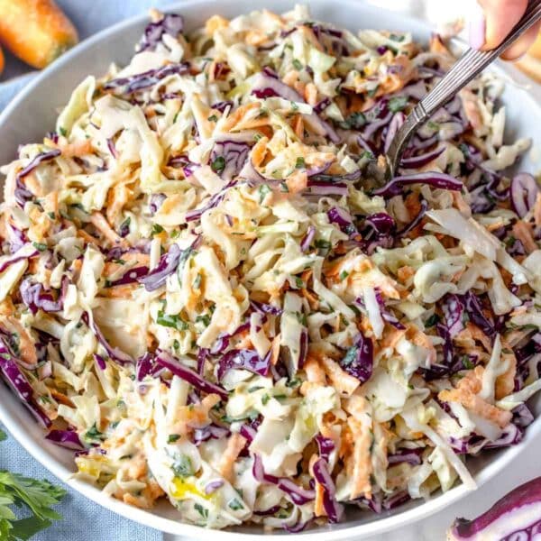 Bowl of healthy coleslaw with Greek yogurt surrounded by ingredients on a wooden table.