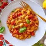 Cherry tomato orzo served on a white plate with basil and lemon zest.