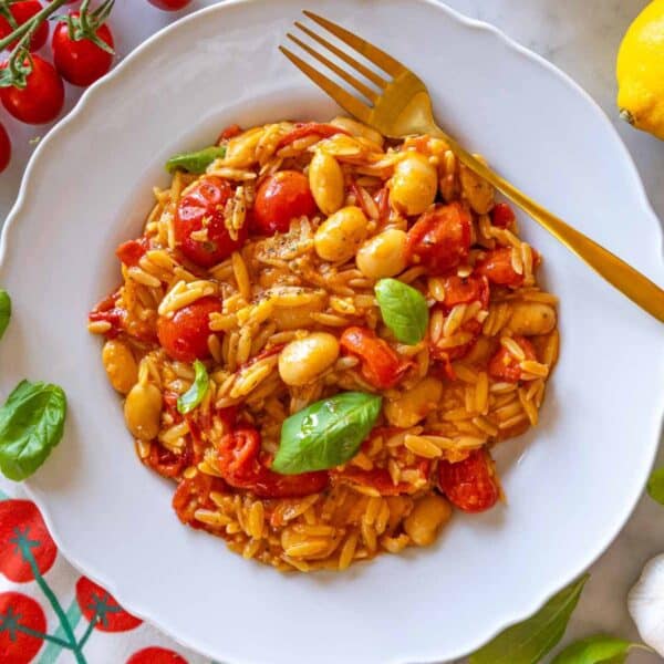 Cherry tomato orzo served on a white plate with basil and lemon zest.
