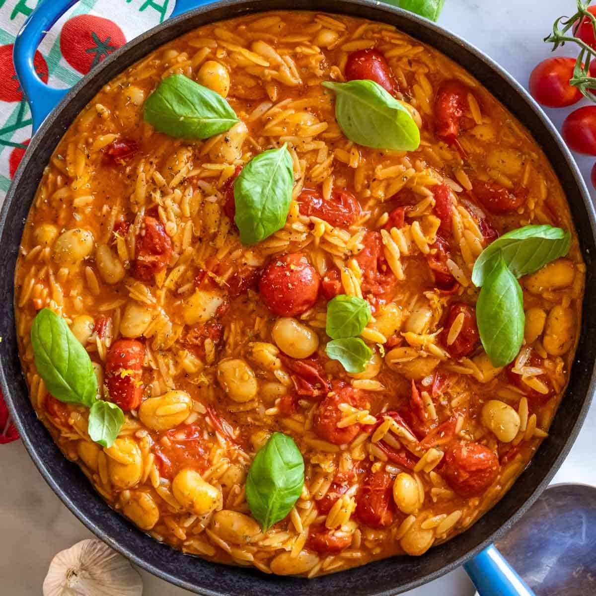 Cherry tomato orzo with butter beans parmesan and basil served in a rustic skillet.