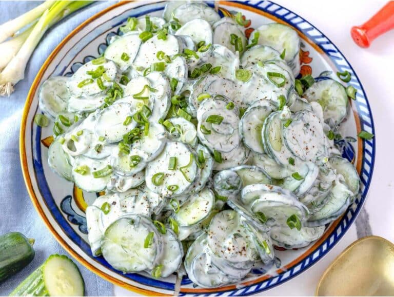 Chilled creamy cucumber salad with Greek yogurt in a serving bowl garnished with scallion tops.