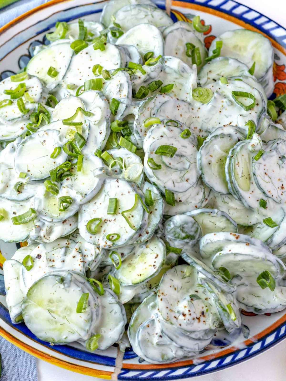 Close up of creamy cucumber salad with yogurt dressing showing cucumber slices and dill.