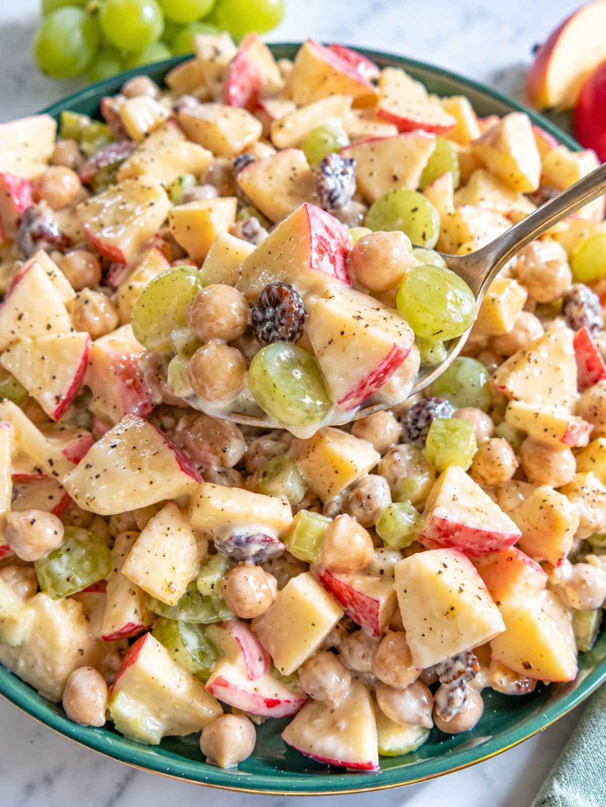 Close-up of glossy apple chickpea salad coated in creamy yogurt dressing with spoon.