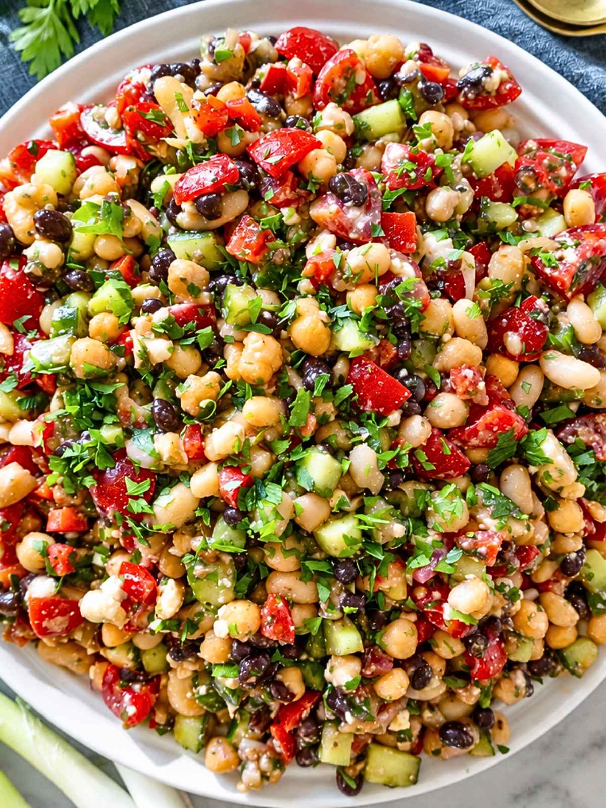 Close-up of glossy marinated beans, crisp vegetables, feta, and fresh parsley.