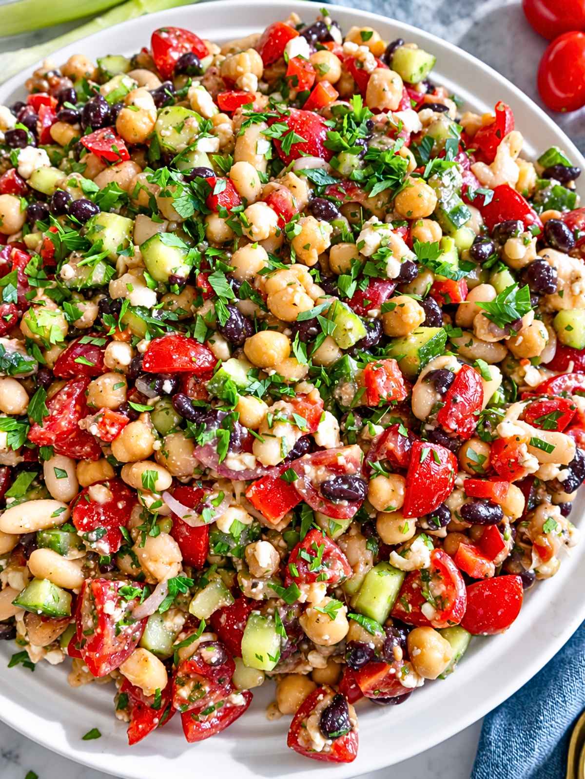 Close-up of glossy marinated beans, vegetables, feta, and fresh parsley.