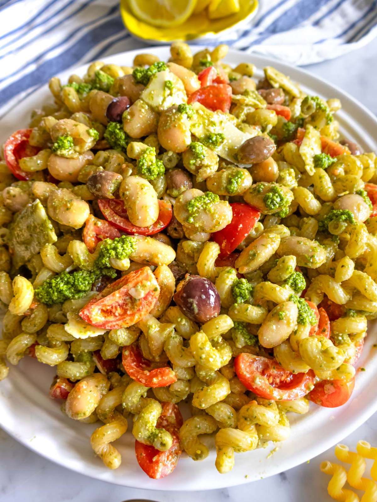 Finished pesto pasta salad with marinated butter beans close up with parmesan and tomatoes.