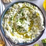 Fresh zucchini tzatziki dip in bowl with olive oil and herb garnish.