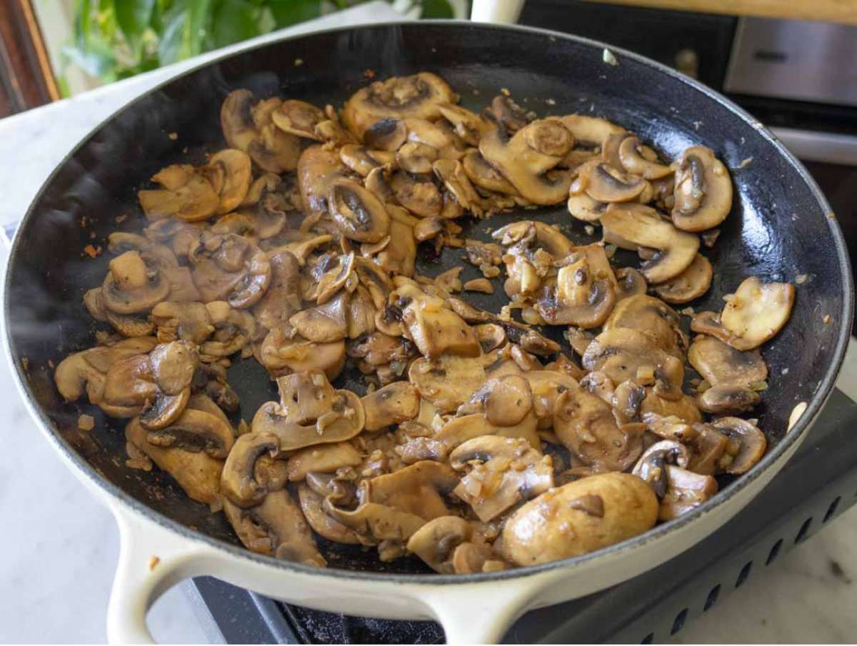 Golden sautéed mushrooms releasing moisture in a skillet for plant-based orzo recipe.