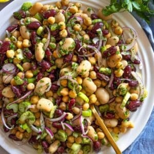 Healthy 3 bean salad recipe on a white platter with fresh parsley and celery.