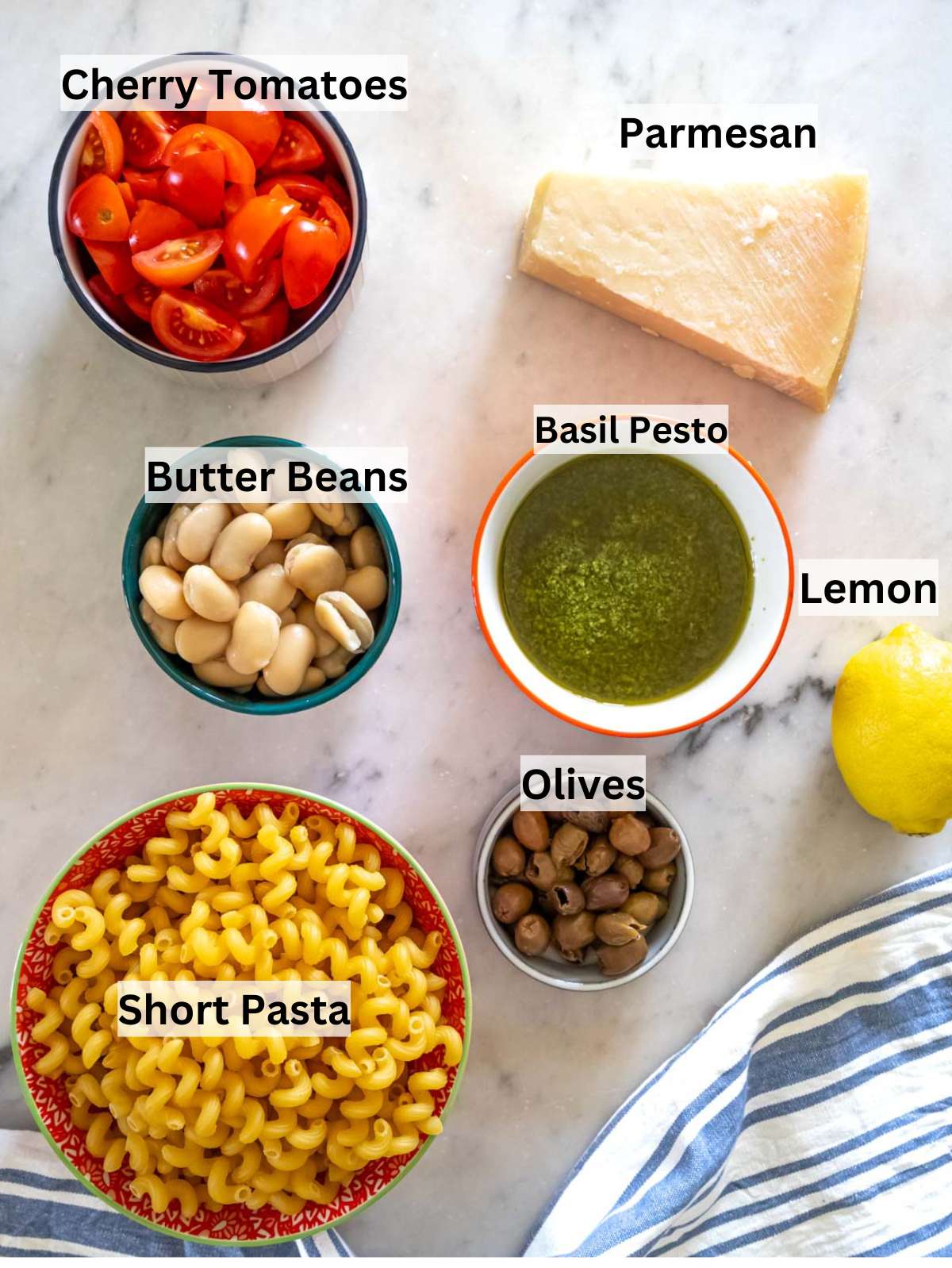 Ingredients for pesto pasta salad with marinated butter beans pasta tomatoes olives parmesan and lemon.