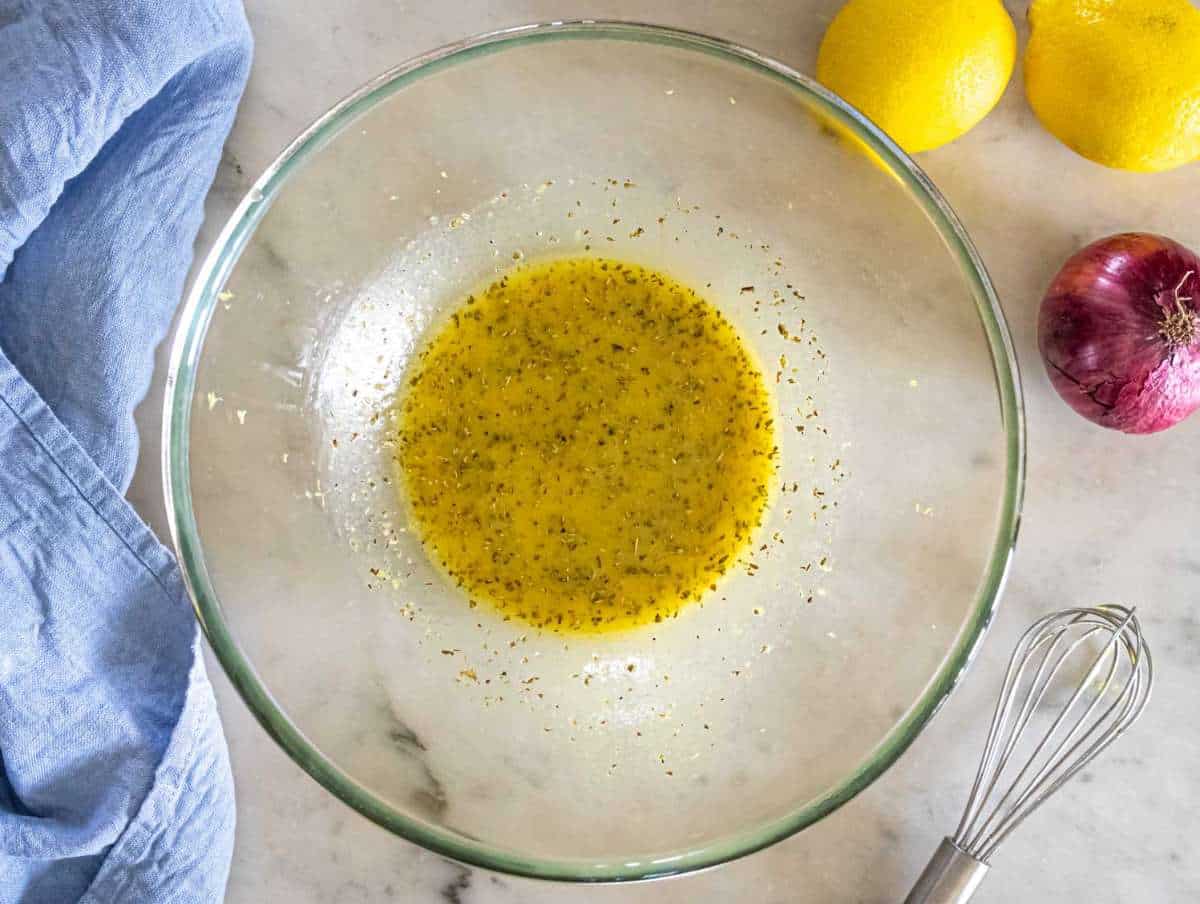 Mixing olive oil vinegar mustard honey garlic and oregano for salad dressing.