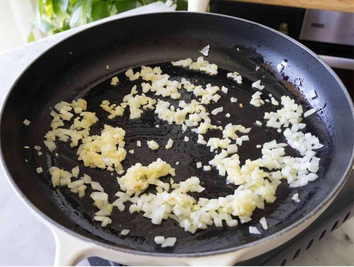 Onions and garlic sautéing in olive oil in a large pan for mushroom orzo recipe.