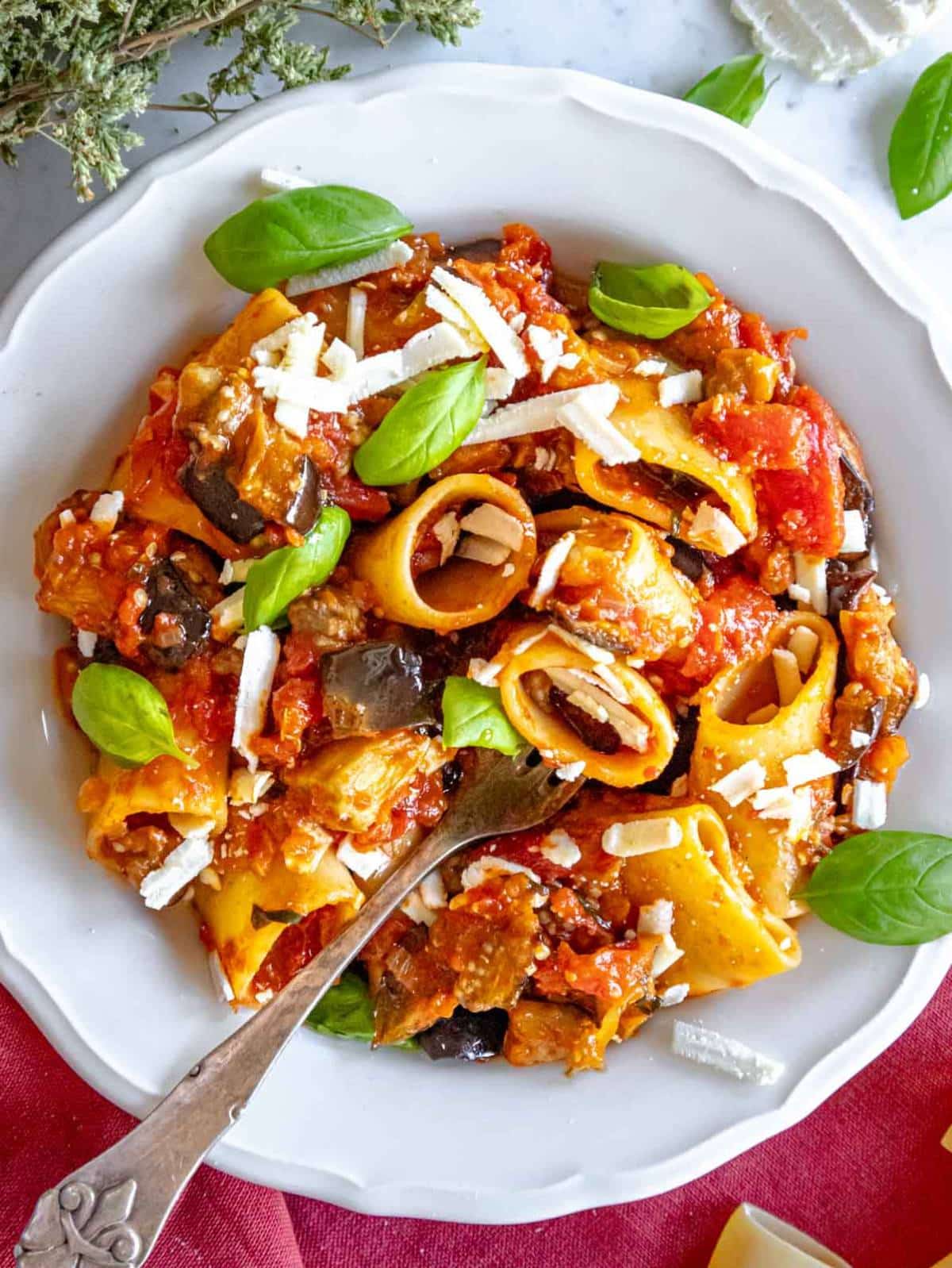 Pasta alla Norma with roasted eggplant tomato sauce and basil on a dinner plate.
