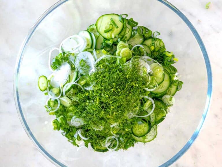 Sliced cucumbers green onion and fresh dill in a mixing bowl ready for cucumber salad.