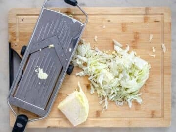 Step 1 Shredding green and red cabbage thinly with a mandoline slicer on a cutting board.