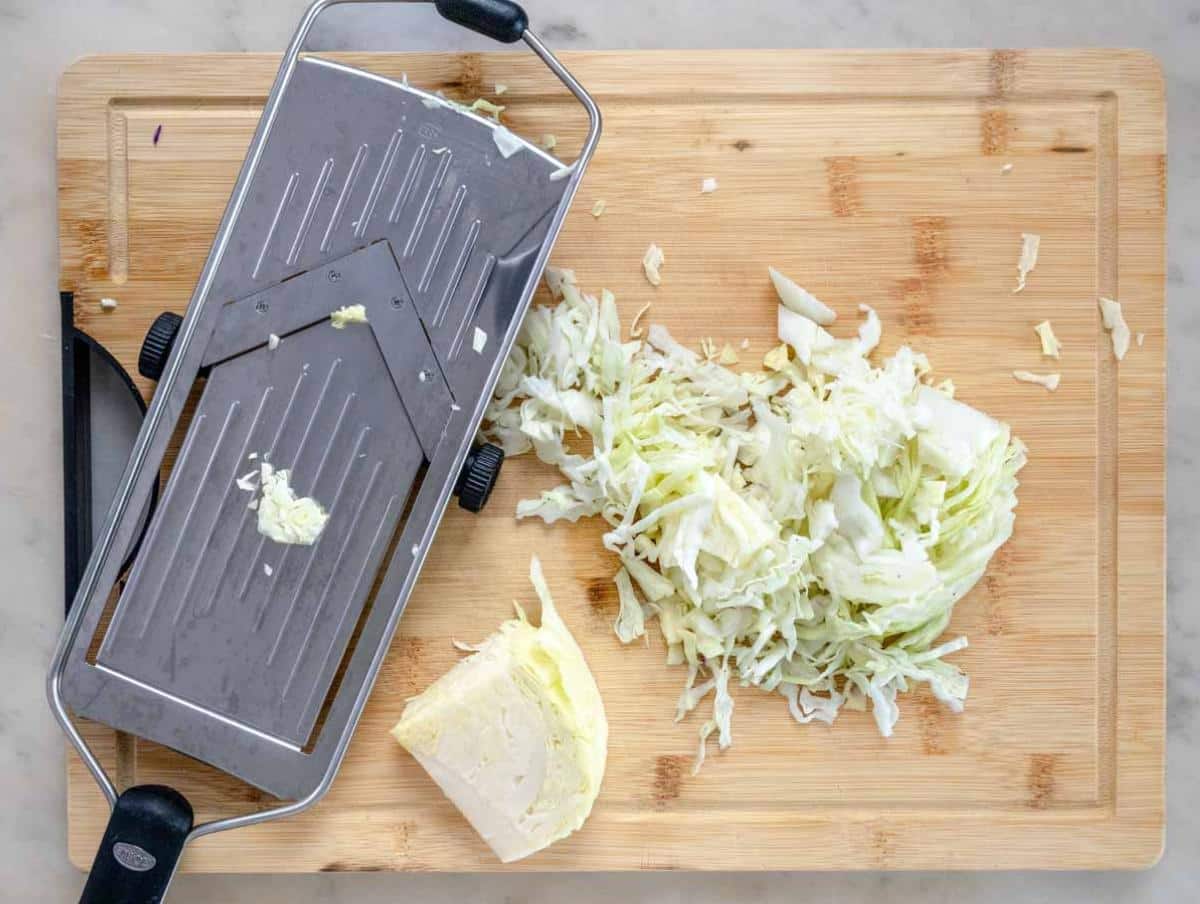 Step 1 Shredding green and red cabbage thinly with a mandoline slicer on a cutting board.