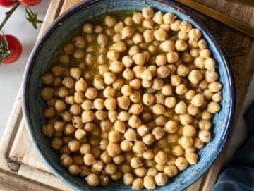 Step 2 Chickpeas tossed in lemon oregano dressing marinating for more flavor in a blue bowl.
