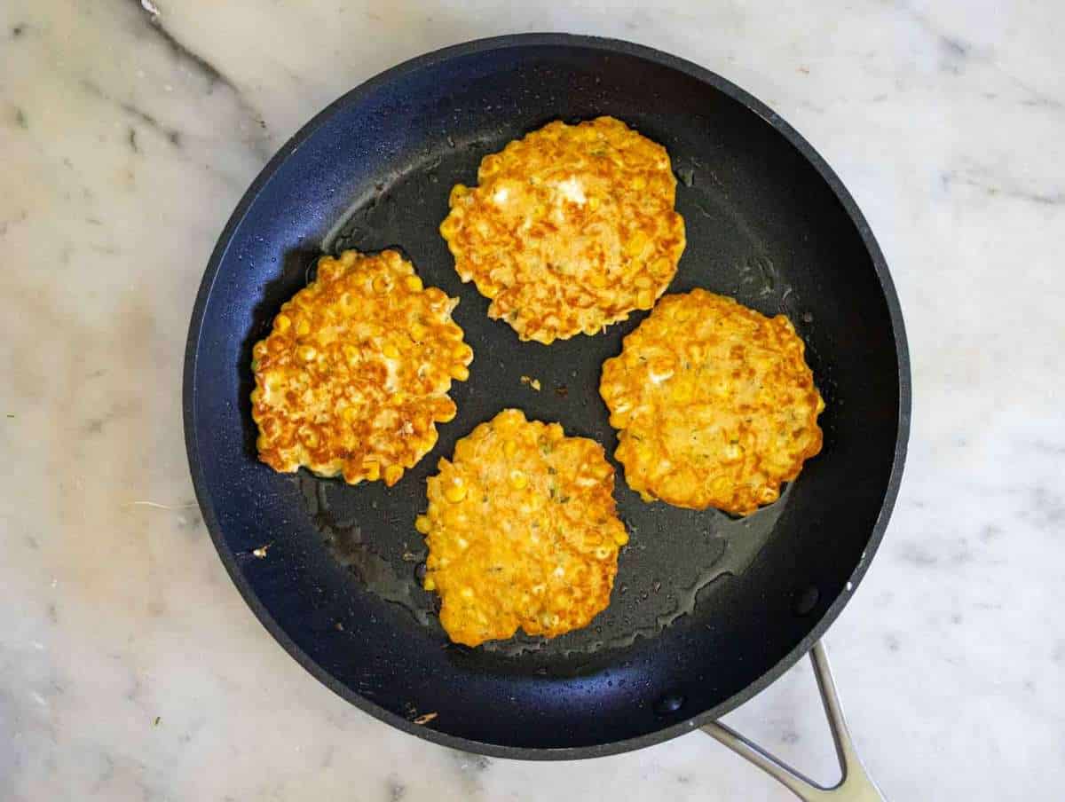 Step 3 Fritters sizzling in a non-stick skillet flattened by a spatula.