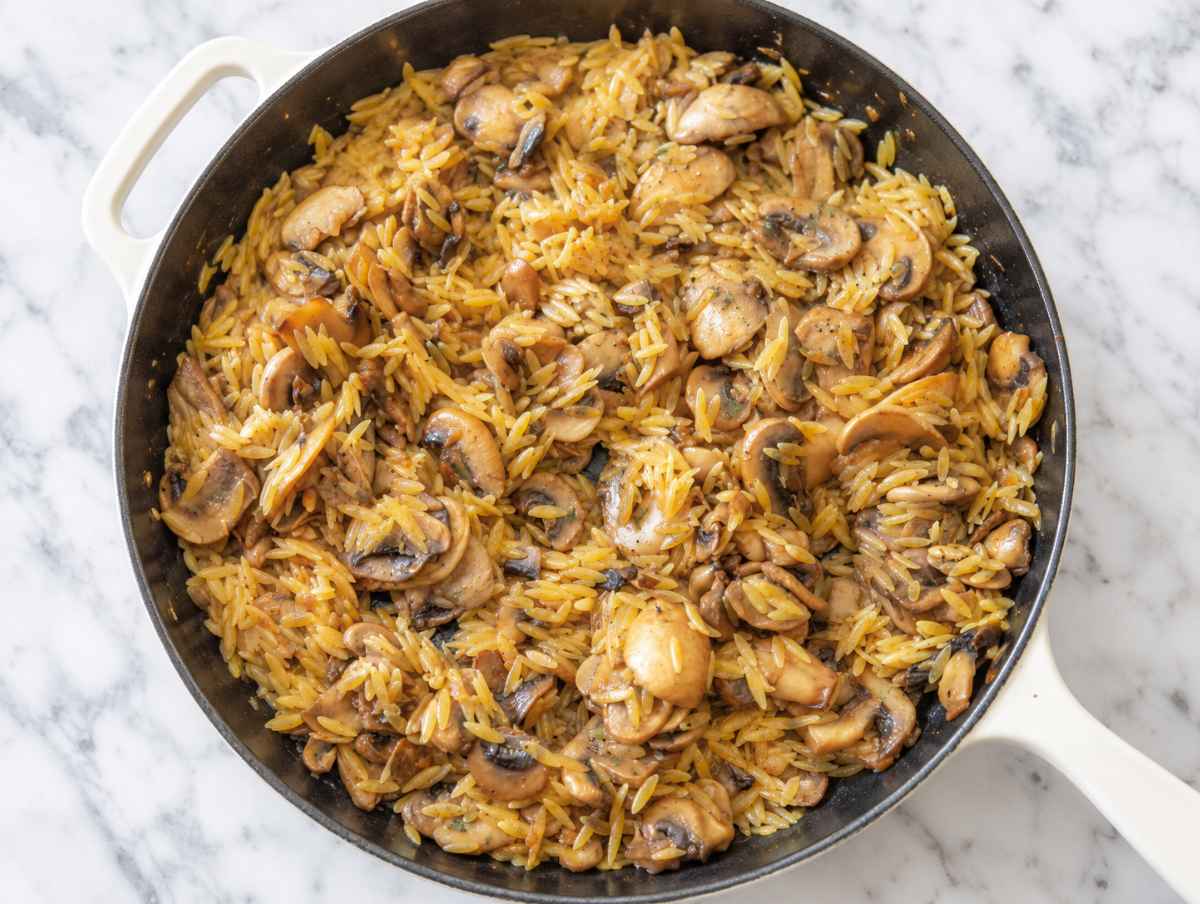 Step 3 Orzo simmering with browned mushrooms and vegetable broth in the skillet.