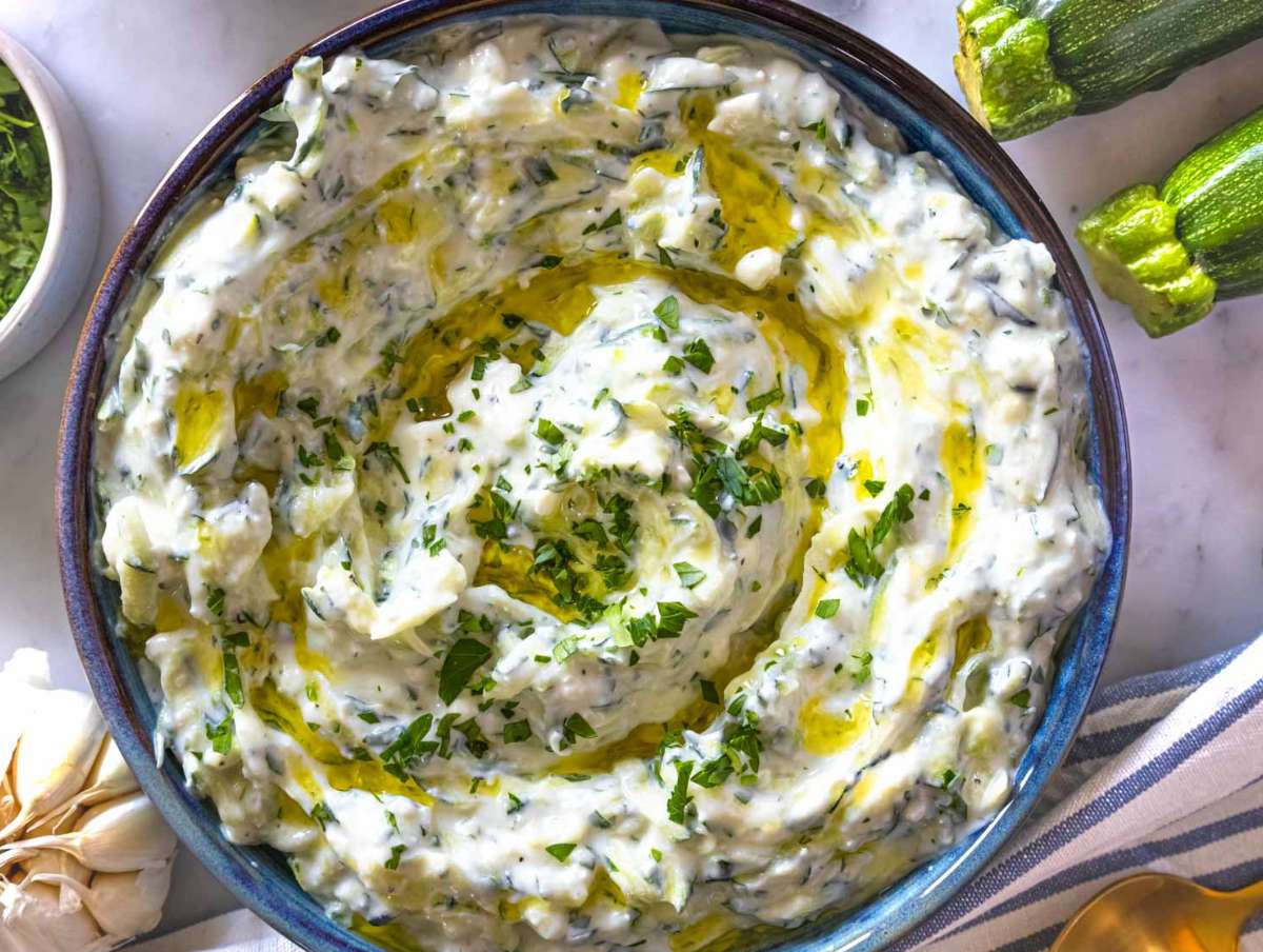 Step 3 Serving the zucchini tzatziki in a blue bowl with a drizzle of oil and fresh herbs.