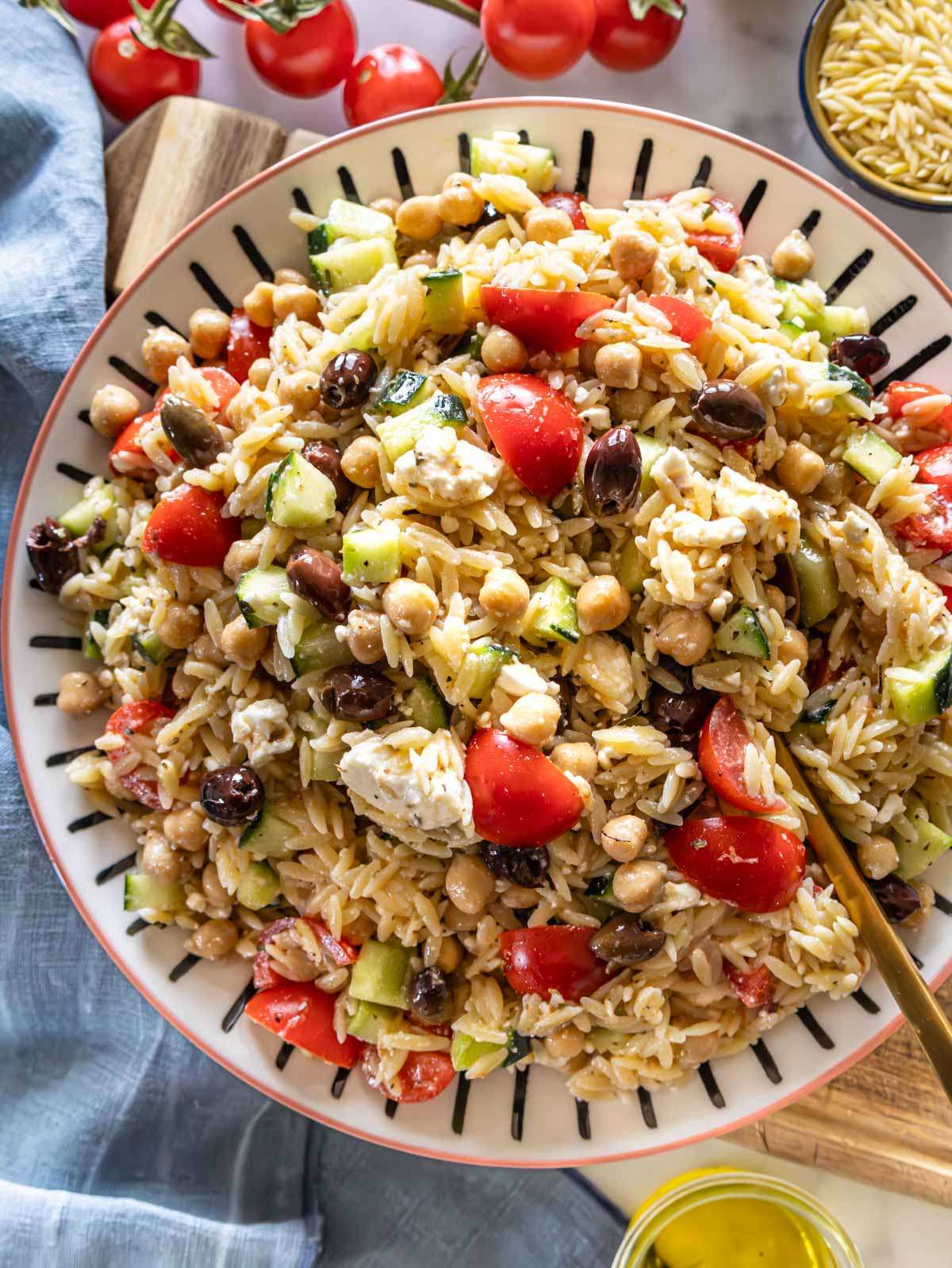 Top down Greek Orzo Salad with tomatoes cucumber olives and marinated chickpeas on serving platter.