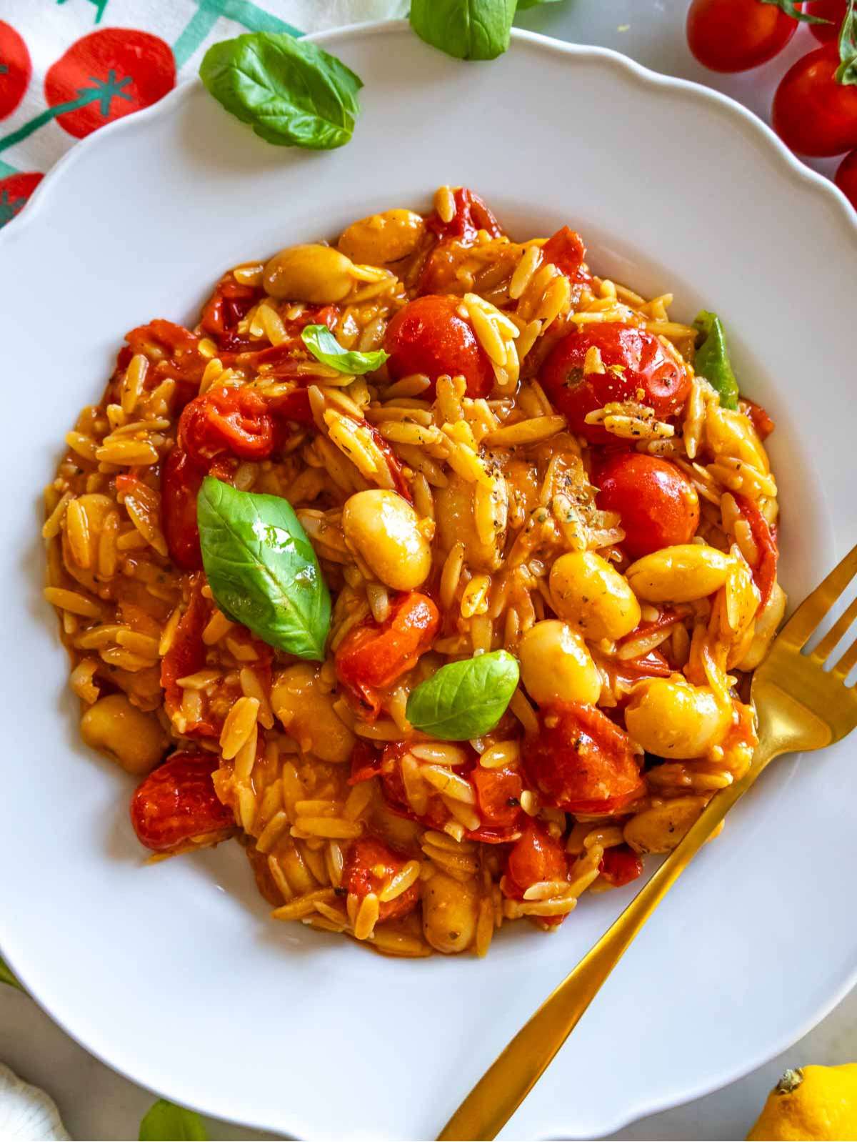 Top-down view of cherry tomato orzo on a plate with lemon zest and herbs.