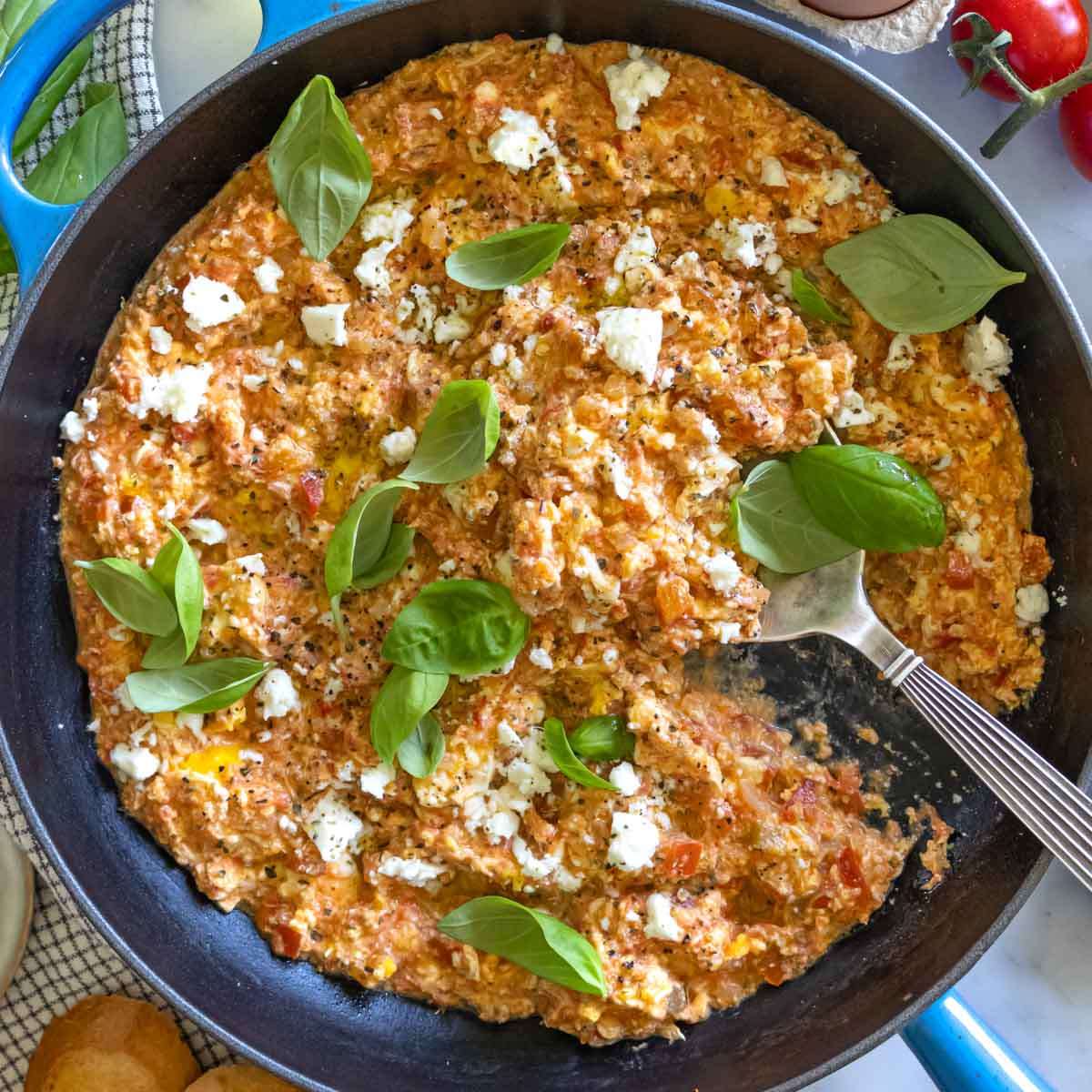 Traditional Greek scrambled eggs recipe with tomatoes feta and bread styled on a rustic table.