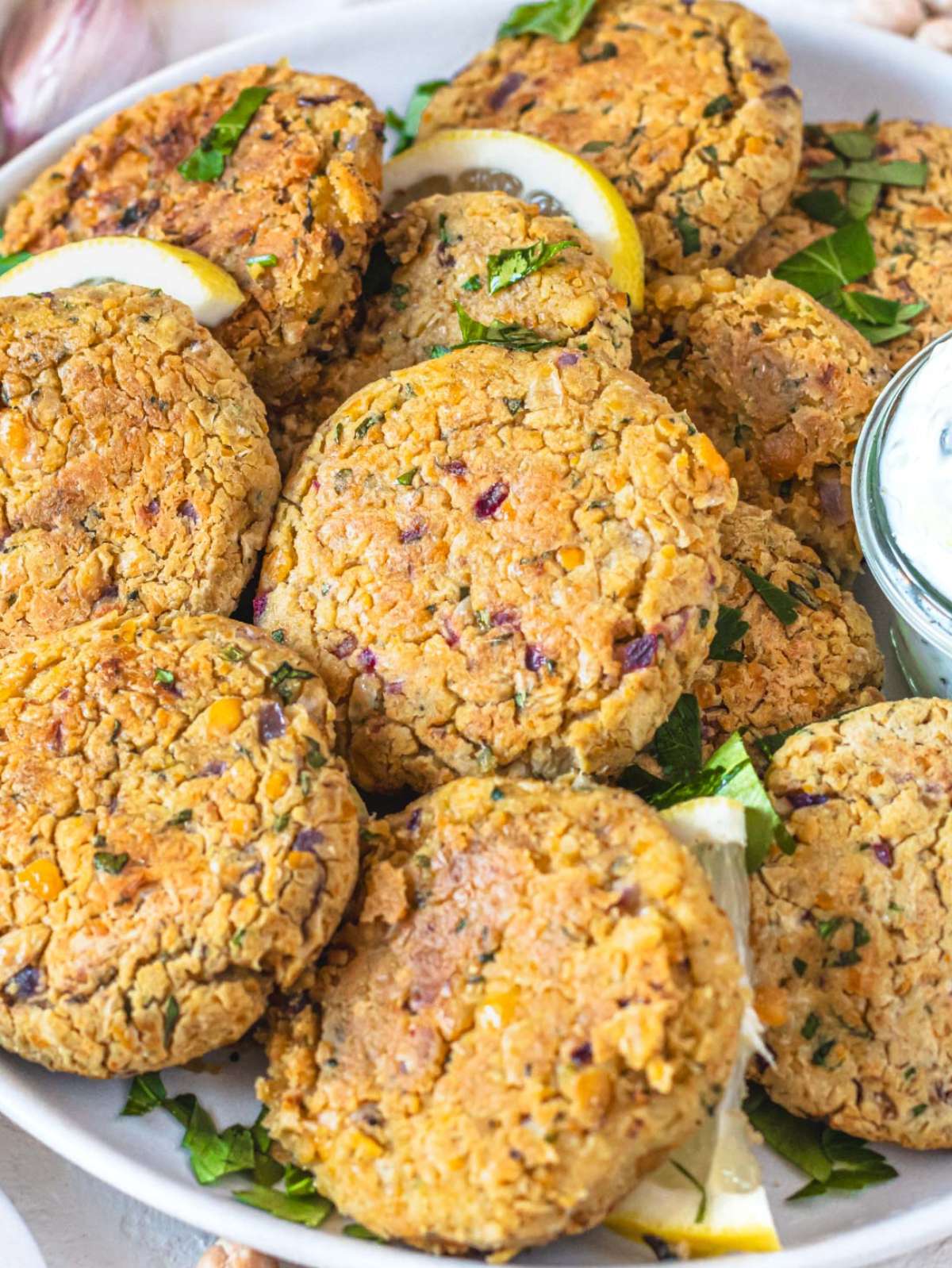 Close up crispy Greek chickpea patties stacked on a plate with fresh herbs.