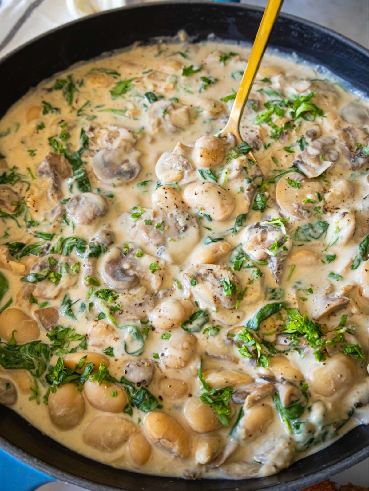 Creamy Marsala butter beans with mushrooms and spinach served in a skillet close up view.