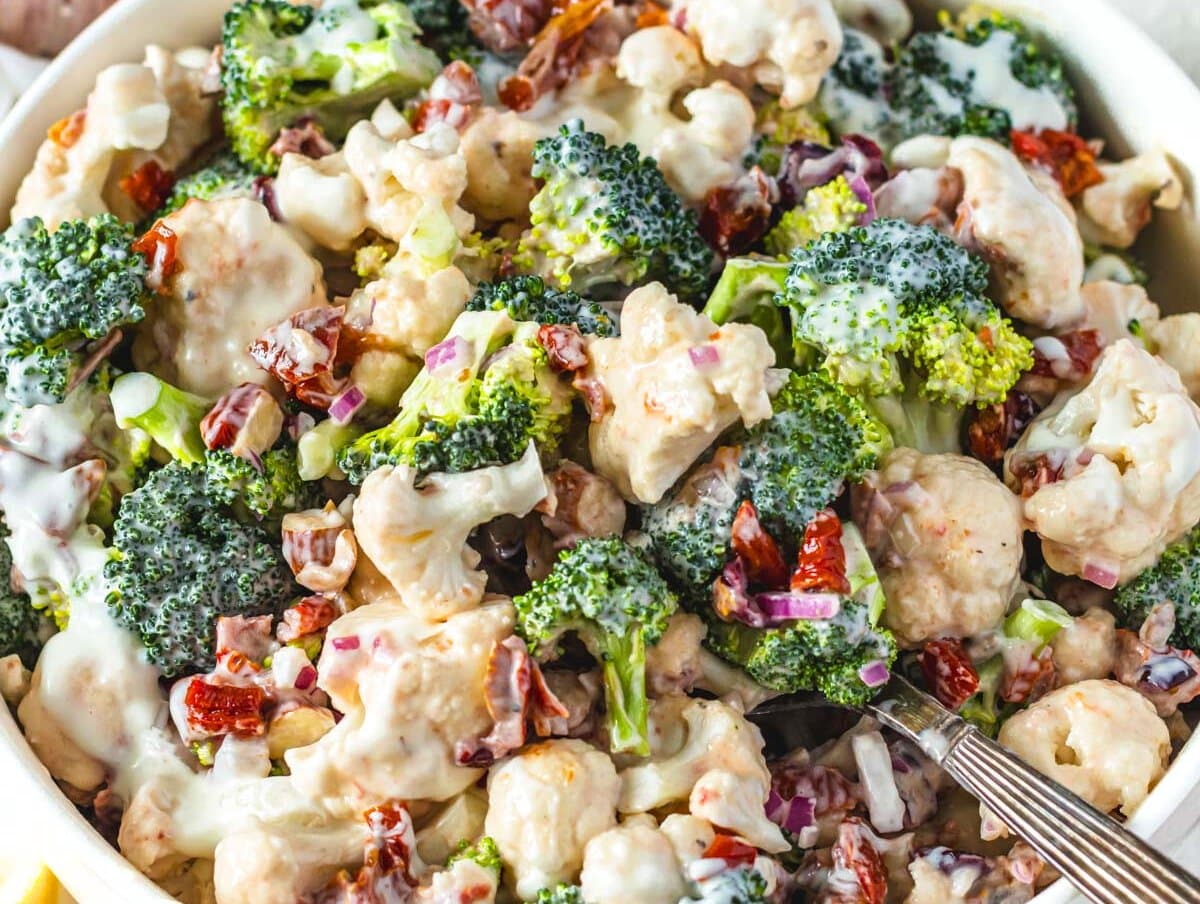 Creamy healthy broccoli cauliflower salad topped with almonds cranberries and sunflower seeds.
