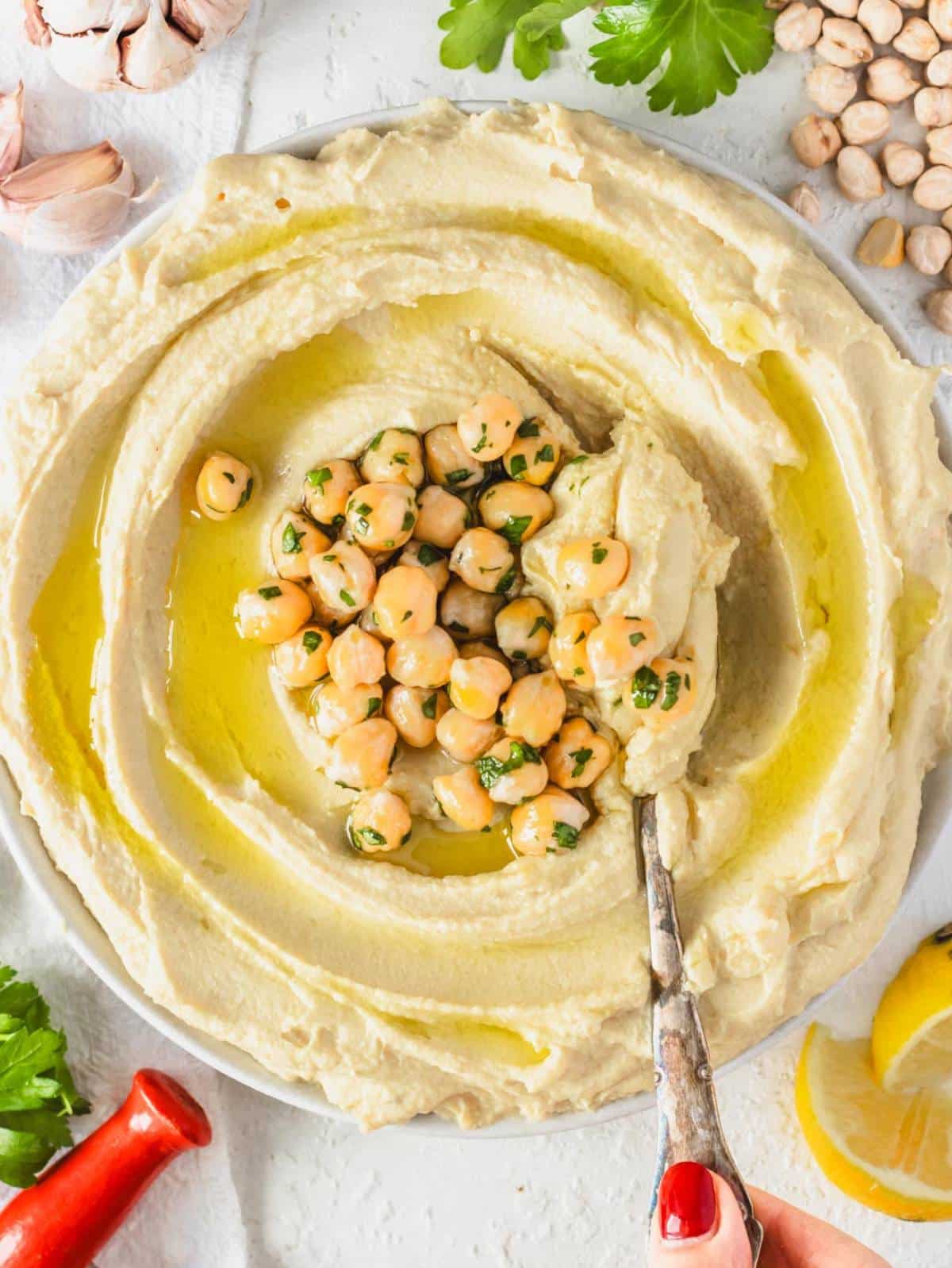 Creamy homemade hummus recipe with canned chickpeas topped with olive oil, chickpeas, and parsley top down.