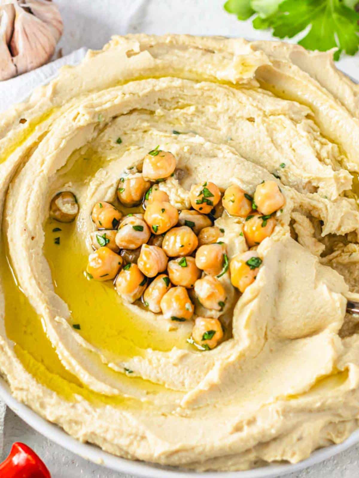 Easy hummus recipe with canned chickpeas served in a bowl garnished with chickpeas and fresh herbs close up.