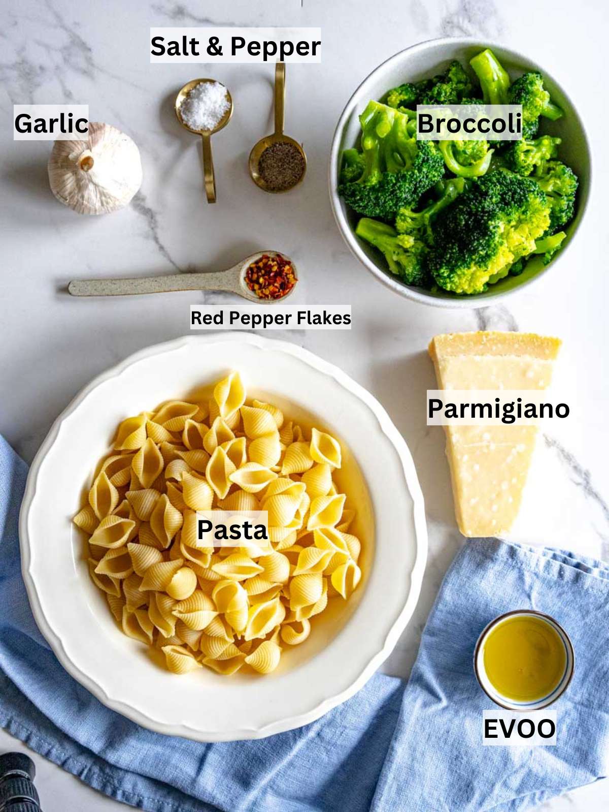 Fresh broccoli pasta garlic parmesan basil and olive oil arranged on a wooden board.