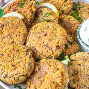 Healthy Greek chickpea patties on a platter with fresh herbs and dipping sauce.