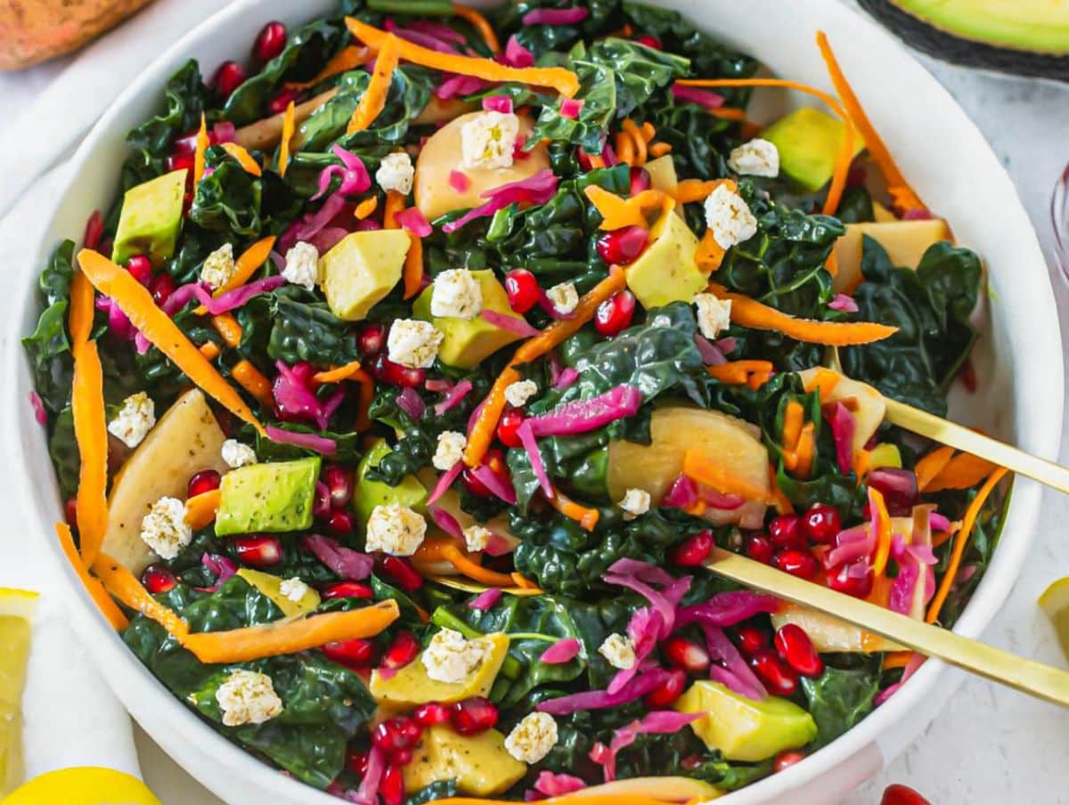 Healthy Mediterranean kale salad topped with feta apple carrot avocado and red cabbage.
